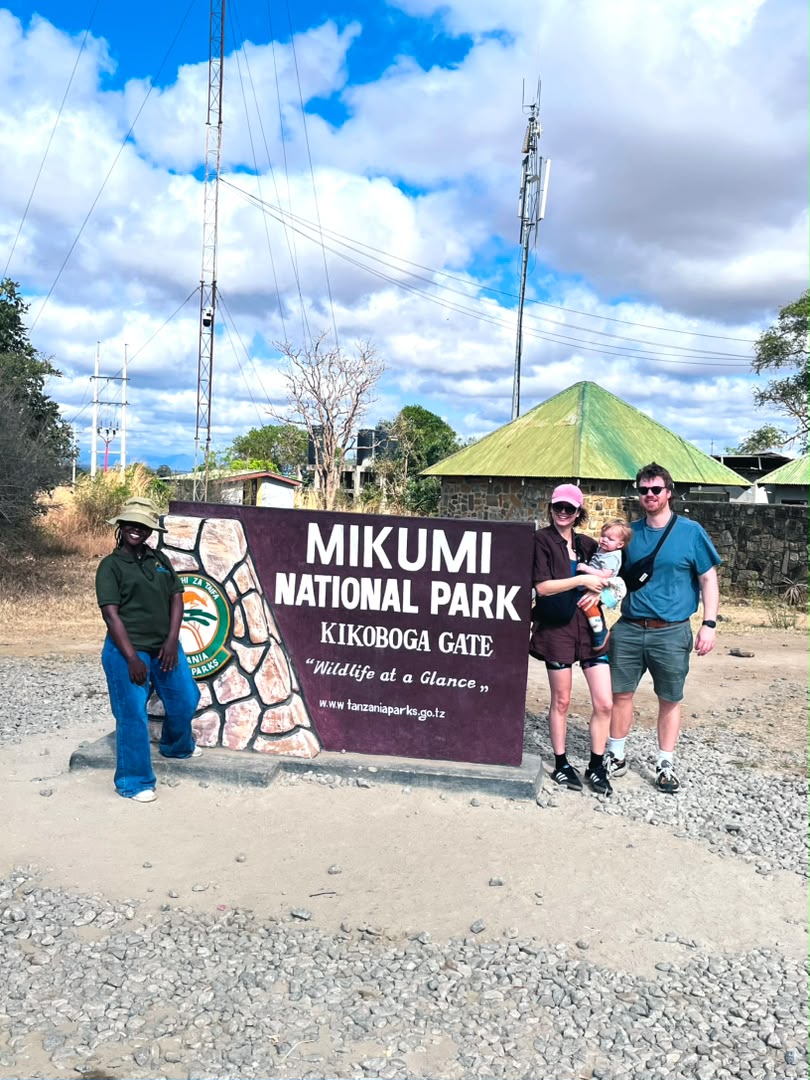 A family with their young child and a Kai Tours guide at the Mikumi National Park Kikoboga Gate sign
